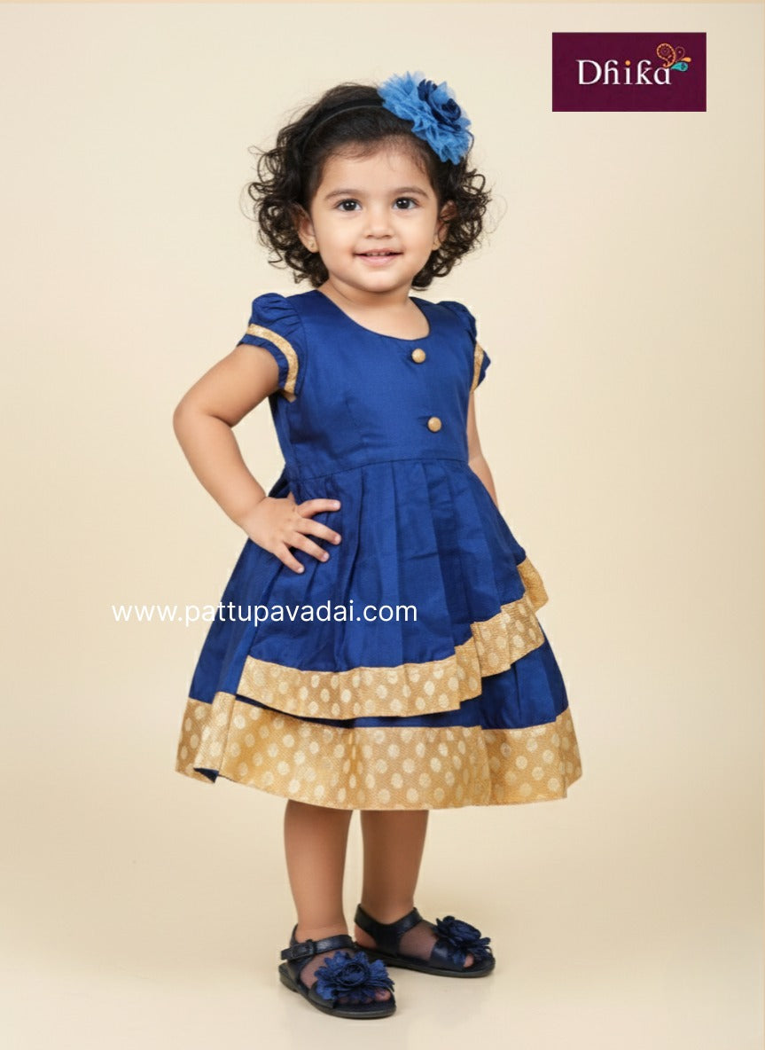 Child wearing a blue and gold dress with a flower in hair, branded 'Dhika'.