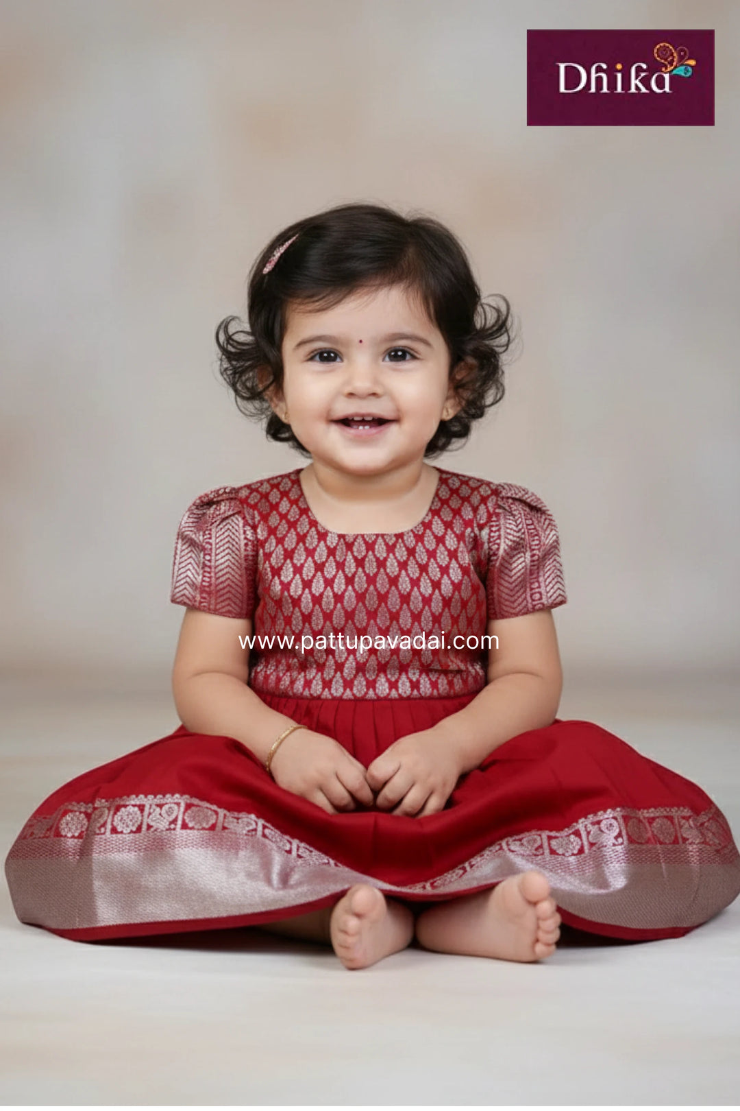 Child wearing a red traditional outfit with a white background, featuring the brand 'Dhika'.
