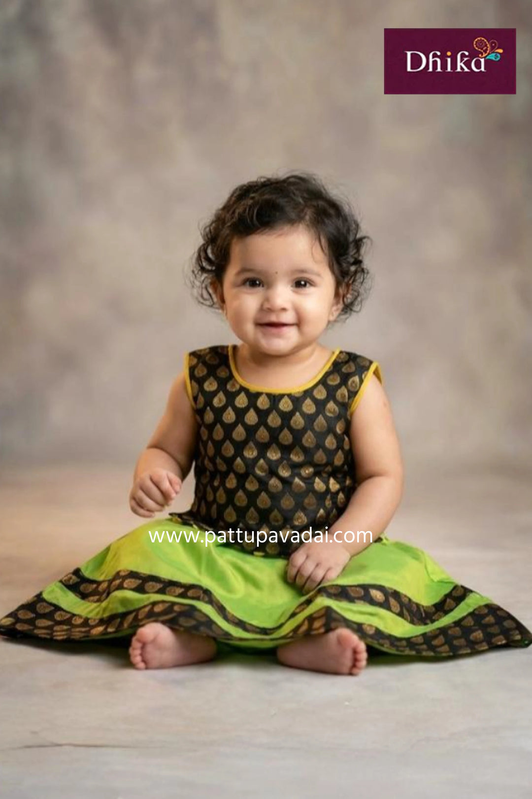 Baby wearing a green and black traditional outfit with 'Dhika' branding.