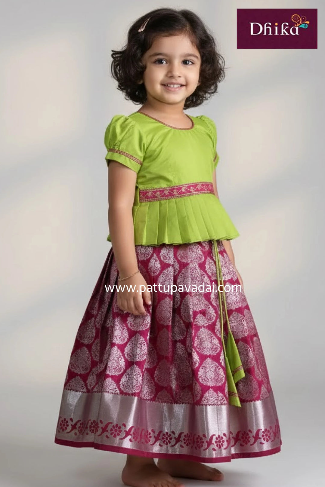 Young girl wearing a green top and pink patterned skirt with 'Dhika' branding.