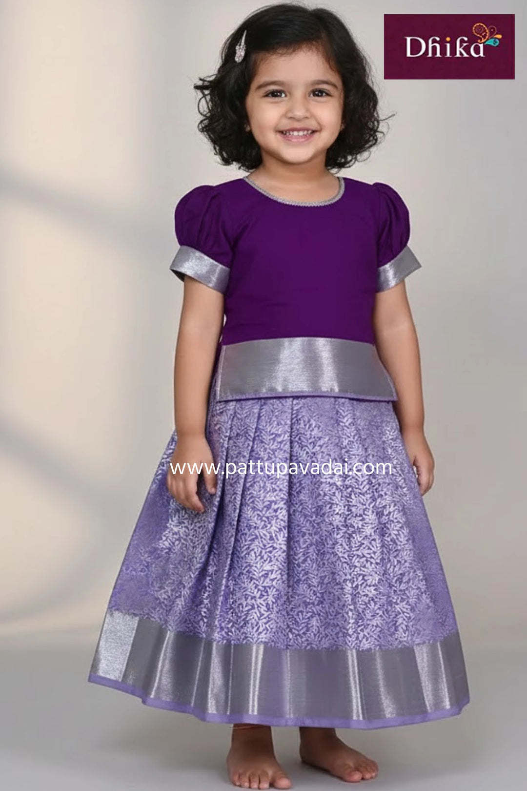 Child wearing a purple dress with silver accents, standing against a plain background.