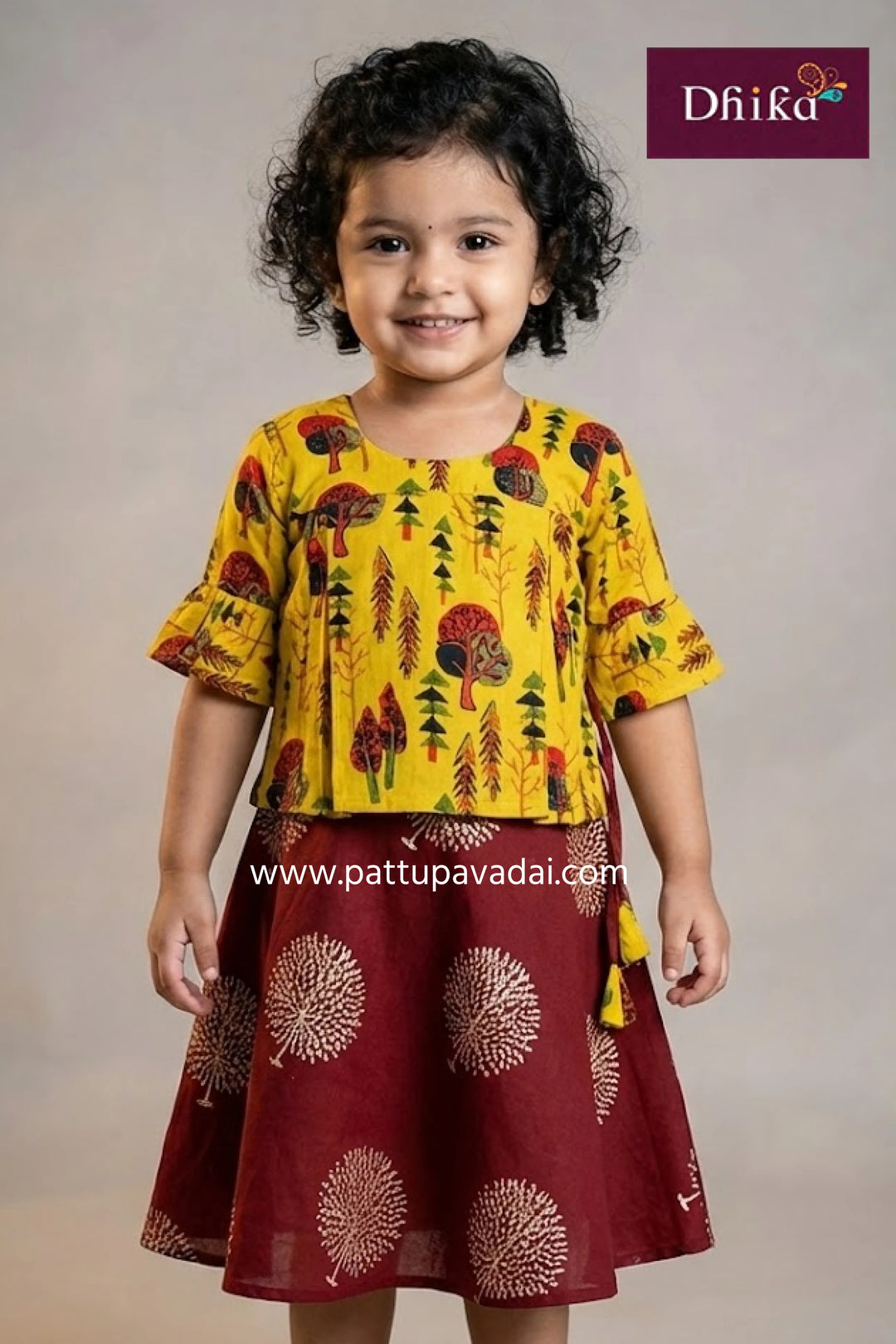 Child wearing a yellow and red traditional outfit with 'Dhika' branding.