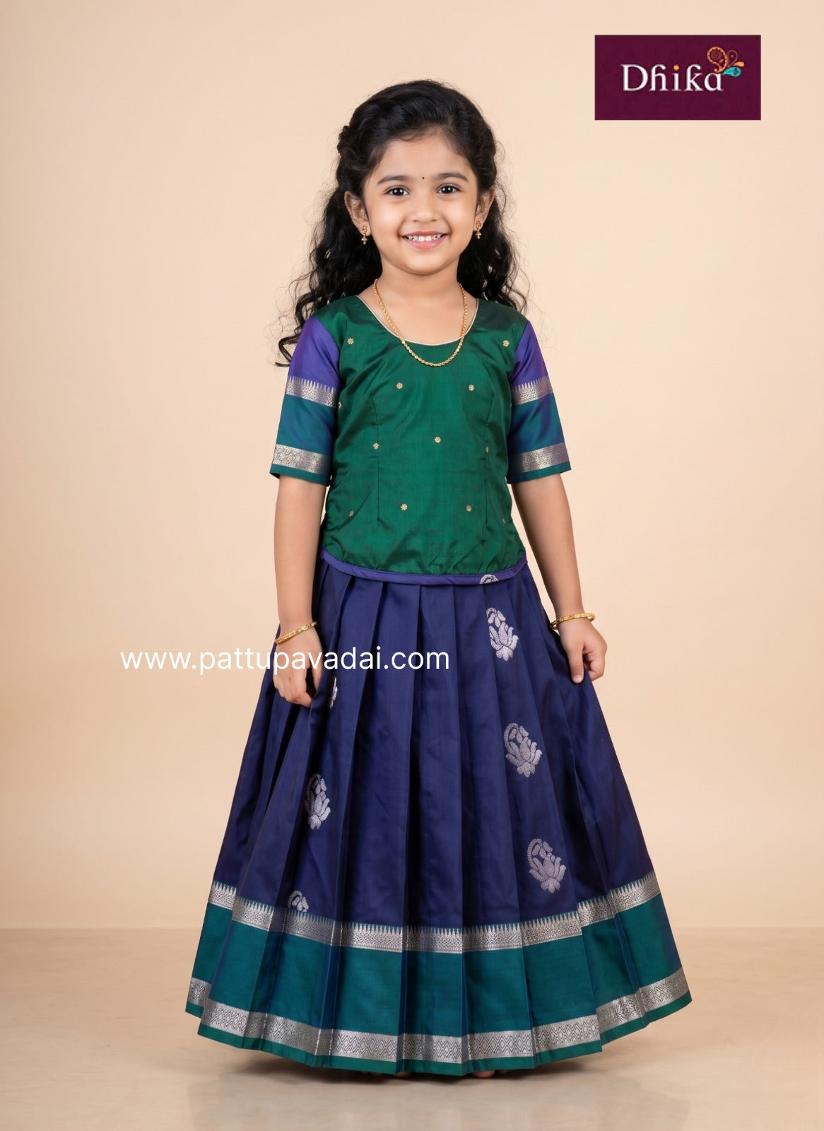 Young girl wearing a green and navy traditional outfit with 'Dhika' branding.