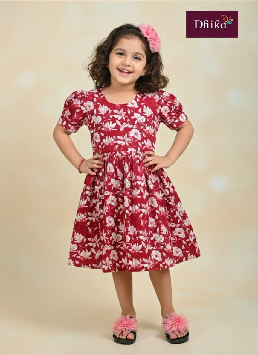 Young girl wearing a red floral dress with a 'Dhika' brand logo.